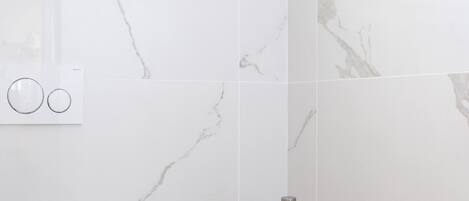 Un baño con inodoro, bidé y lavamanos, paredes de mármol y un panel de madera.