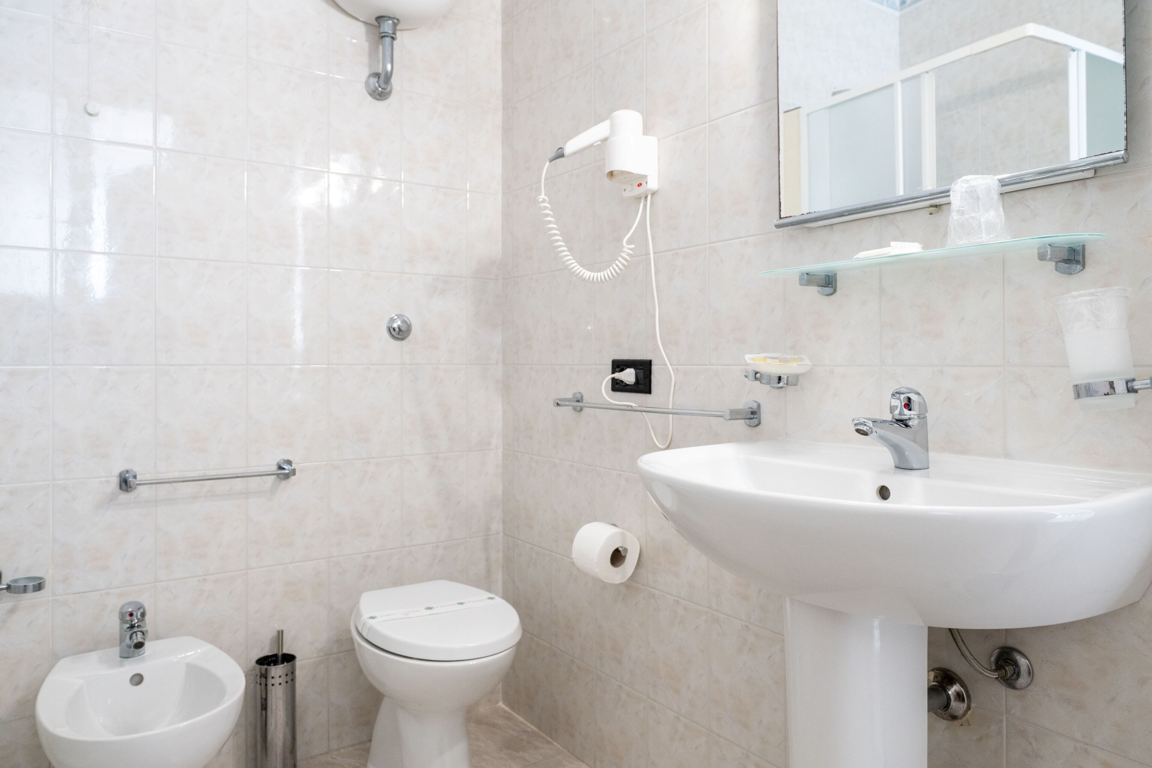 Un baño con lavamanos blanco, inodoro, bidé y un secador de pelo montado en la pared.