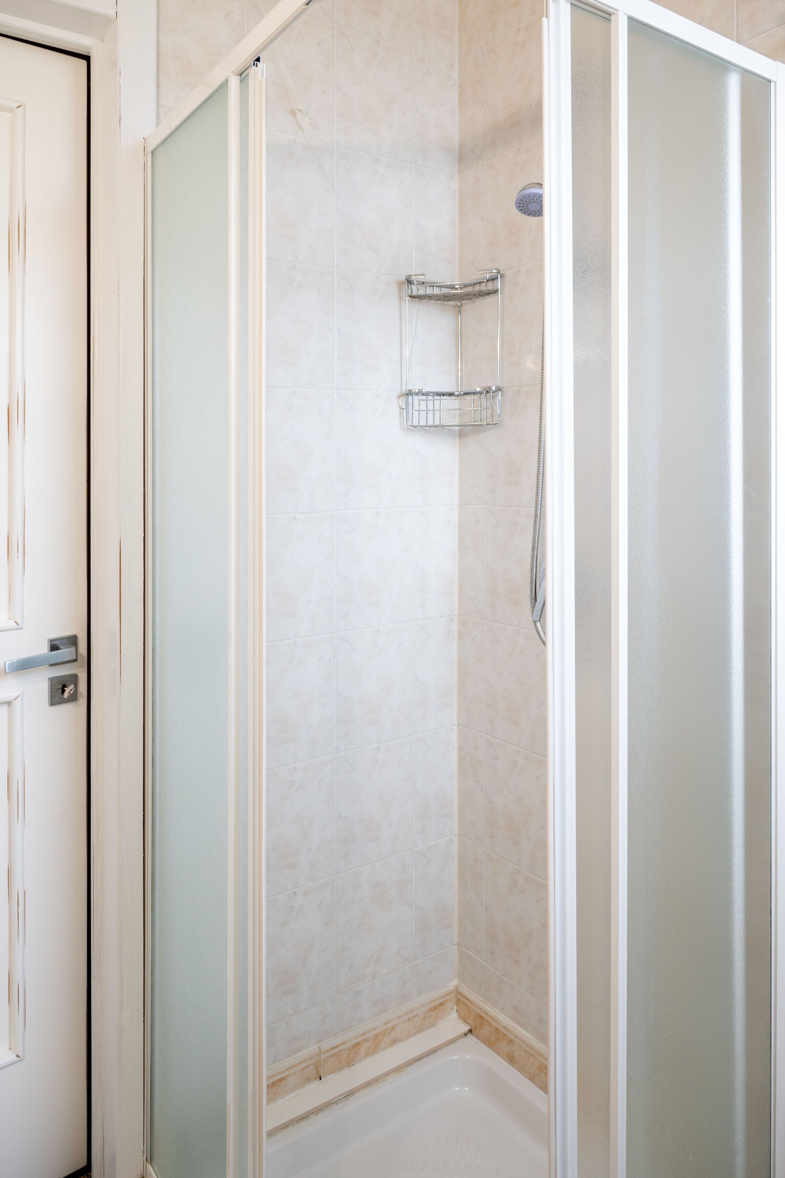 Une salle de bain avec une douche à parois de verre, un sol carrelé et une étagère en métal.