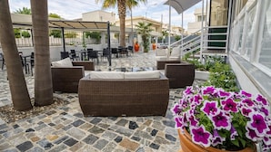An outdoor seating area with wicker furniture, a palm tree, and a potted plant with purple flowers. - Hotiday Porto Cesareo (Porto Cesareo)