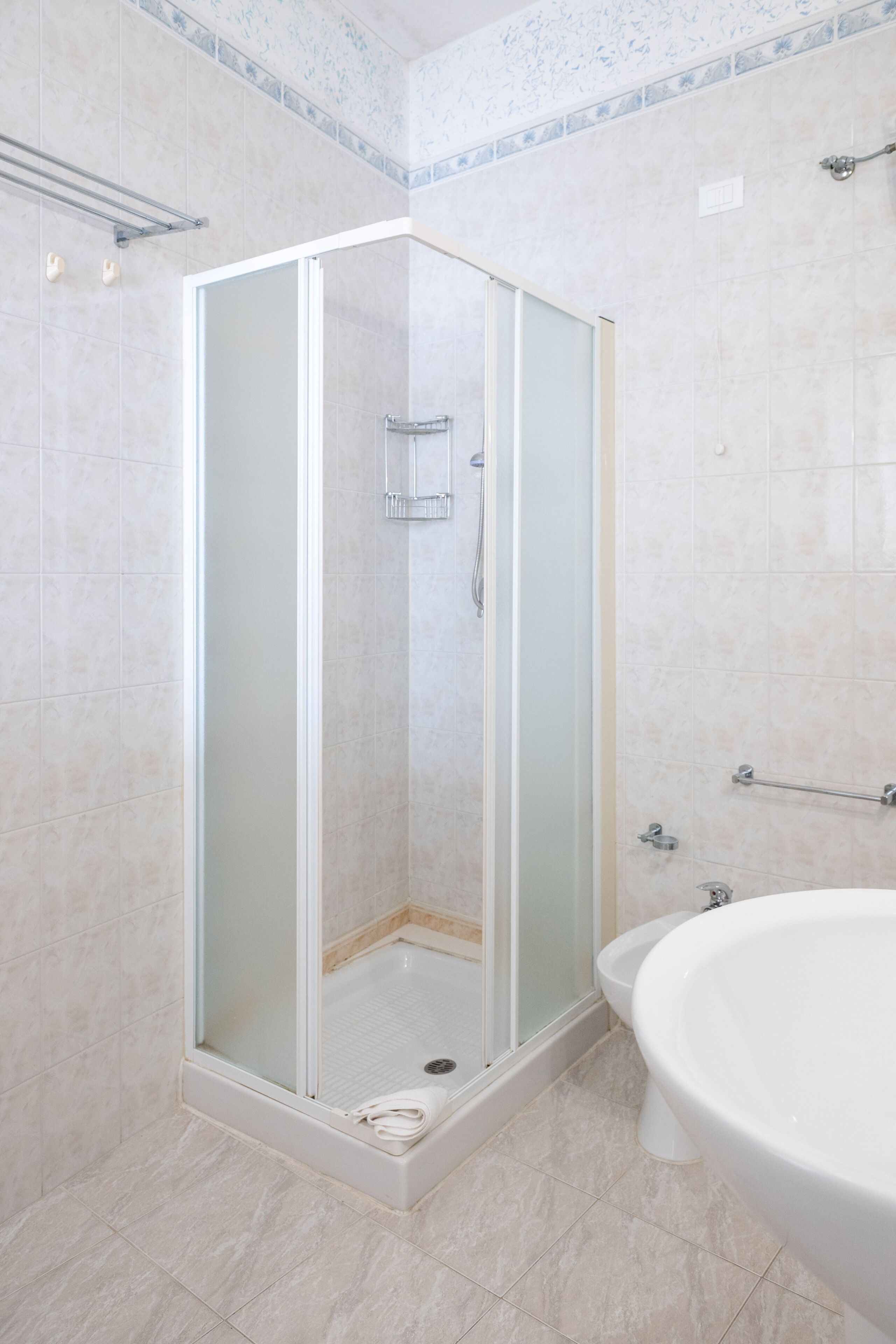 Una doccia con porta in vetro, una vasca da bagno bianca e un pavimento piastrellato.