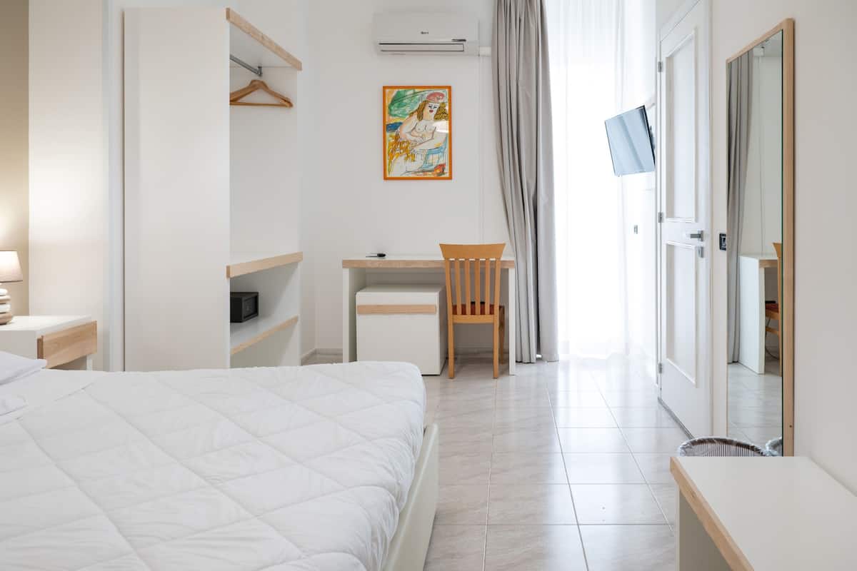 A hotel room with a bed, a desk, a chair, a TV, and a wardrobe.