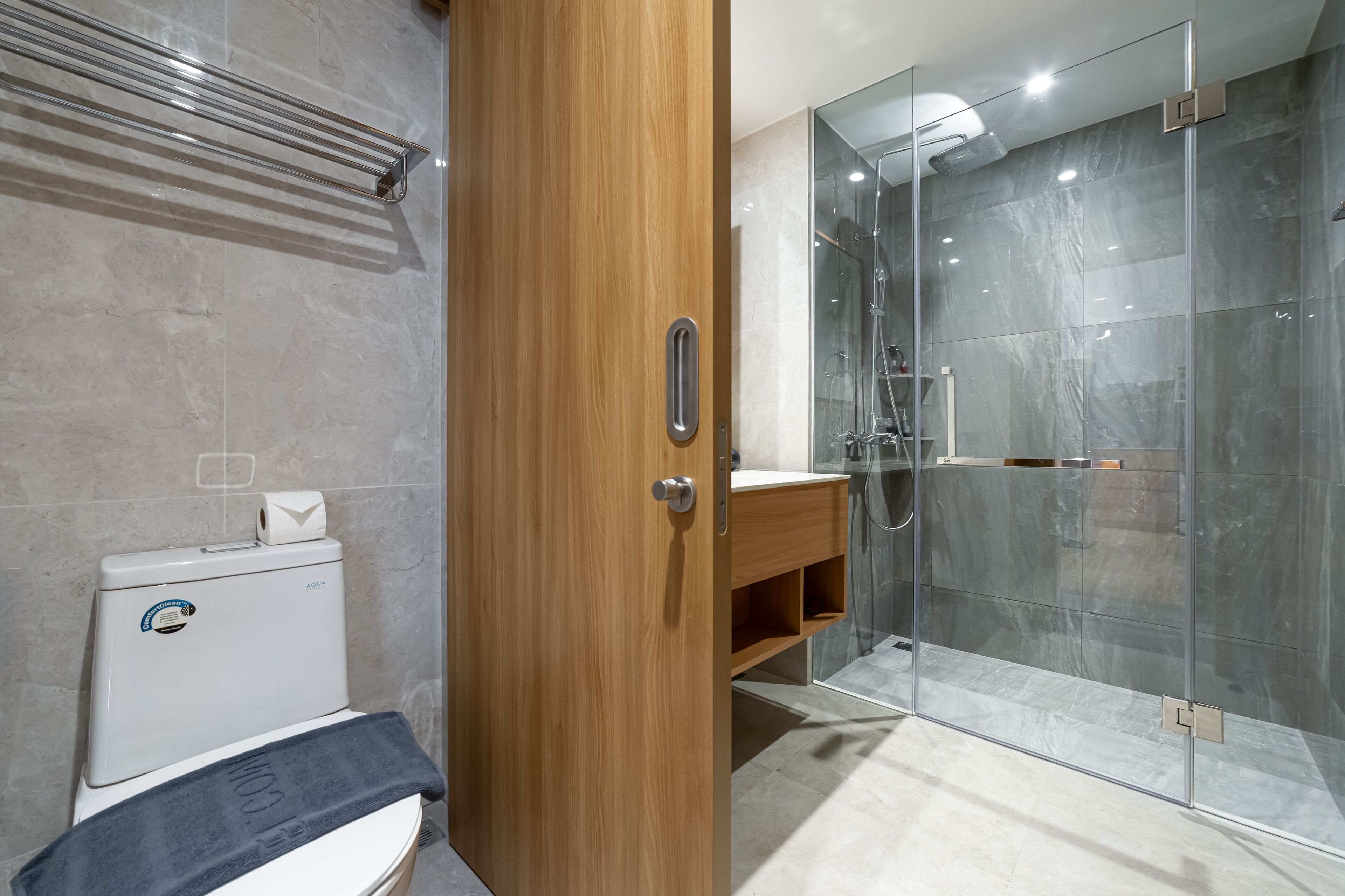 A modern bathroom with a toilet, a towel rack, a glass shower enclosure, and a wooden vanity.