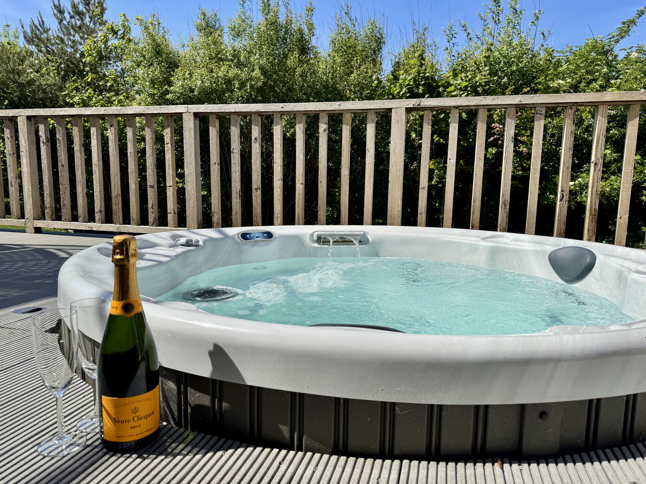 Un jacuzzi con una botella de Veuve Clicquot Brut champagne y dos copas en una terraza.
