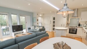 A modern living room with a grey sofa, a flat-screen TV, and a dining table with a decorative centerpiece.