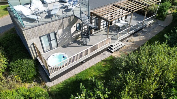 A modern house with a rooftop deck featuring a hot tub, outdoor seating, and a pergola.
