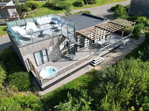 A modern house with a rooftop deck featuring a hot tub, outdoor seating, and a pergola. - The Black Barnacle (Redruth)