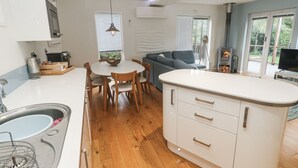 A modern kitchen with a central island, dining table, and chairs. There is a built-in stove, a sink, and a window with blinds.