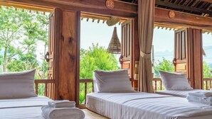 Quarto de madeira com duas camas, cada uma com roupa de cama e almofadas brancas, e vista para o verde lá fora.