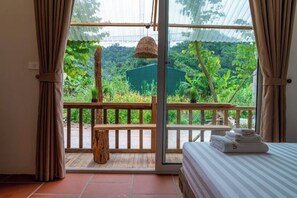 A room with a bed, a bench, and a view of lush greenery through a glass door.