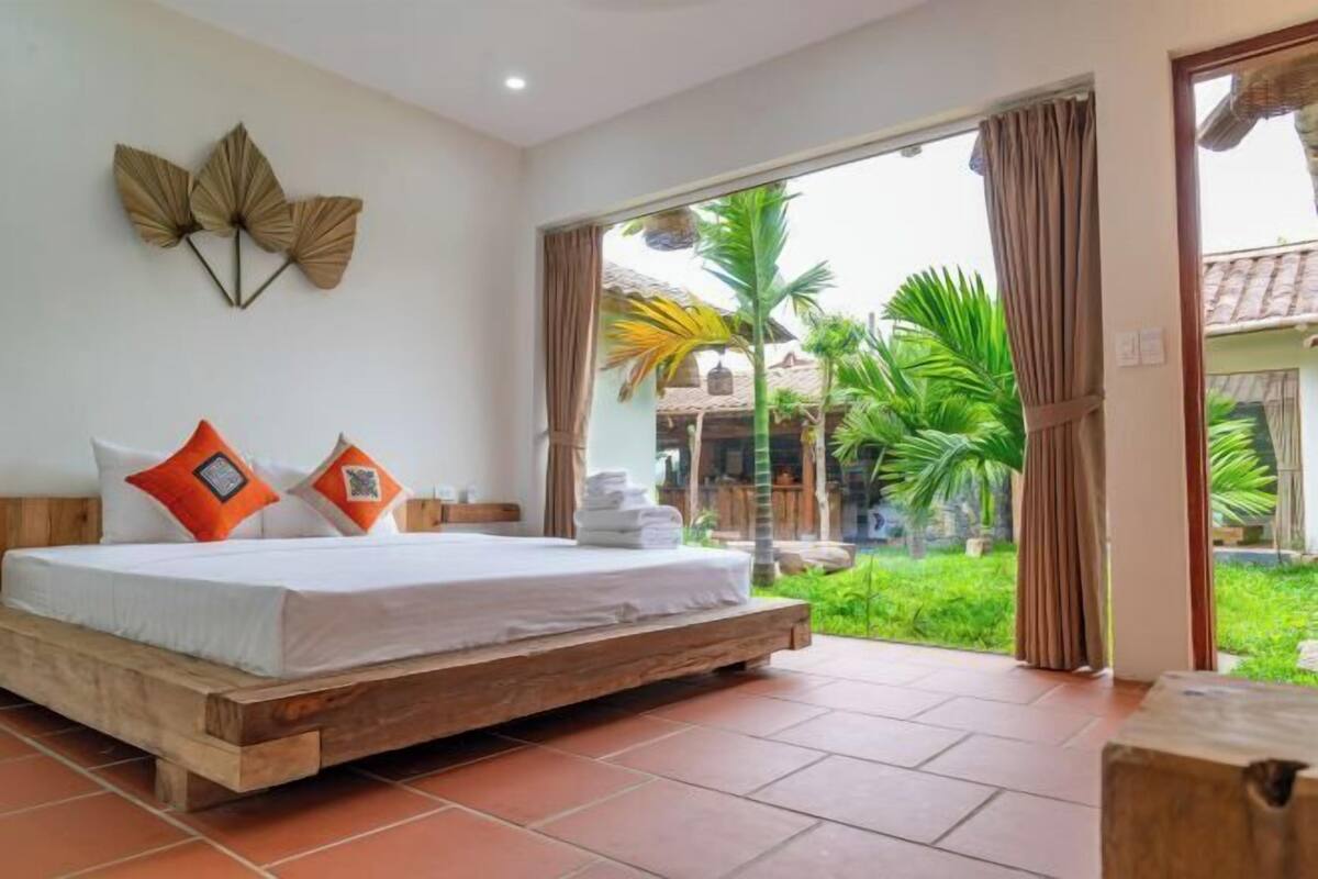A bedroom with a wooden bed, a view of greenery, and a large window.