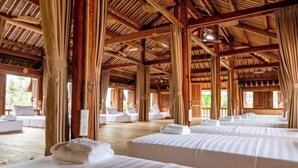 Quarto de hotel com várias camas, vigas de madeira e janelas amplas.