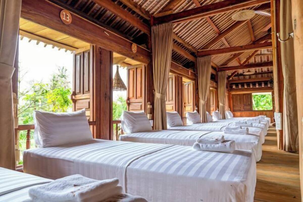 A room with multiple beds, wooden beams, and a view of greenery.