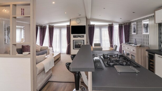 A modern kitchen with a central island, a dining area with a table and chairs, and a living area with a sofa and a TV.