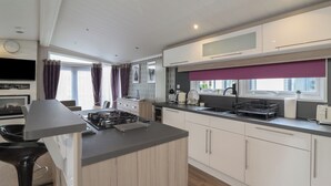 A modern kitchen with a central island, white cabinetry, and a purple window blind.