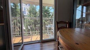 A room with a wooden table and chairs, a sliding glass door leading to an outdoor balcony with a metal railing and a view of trees and buildings.