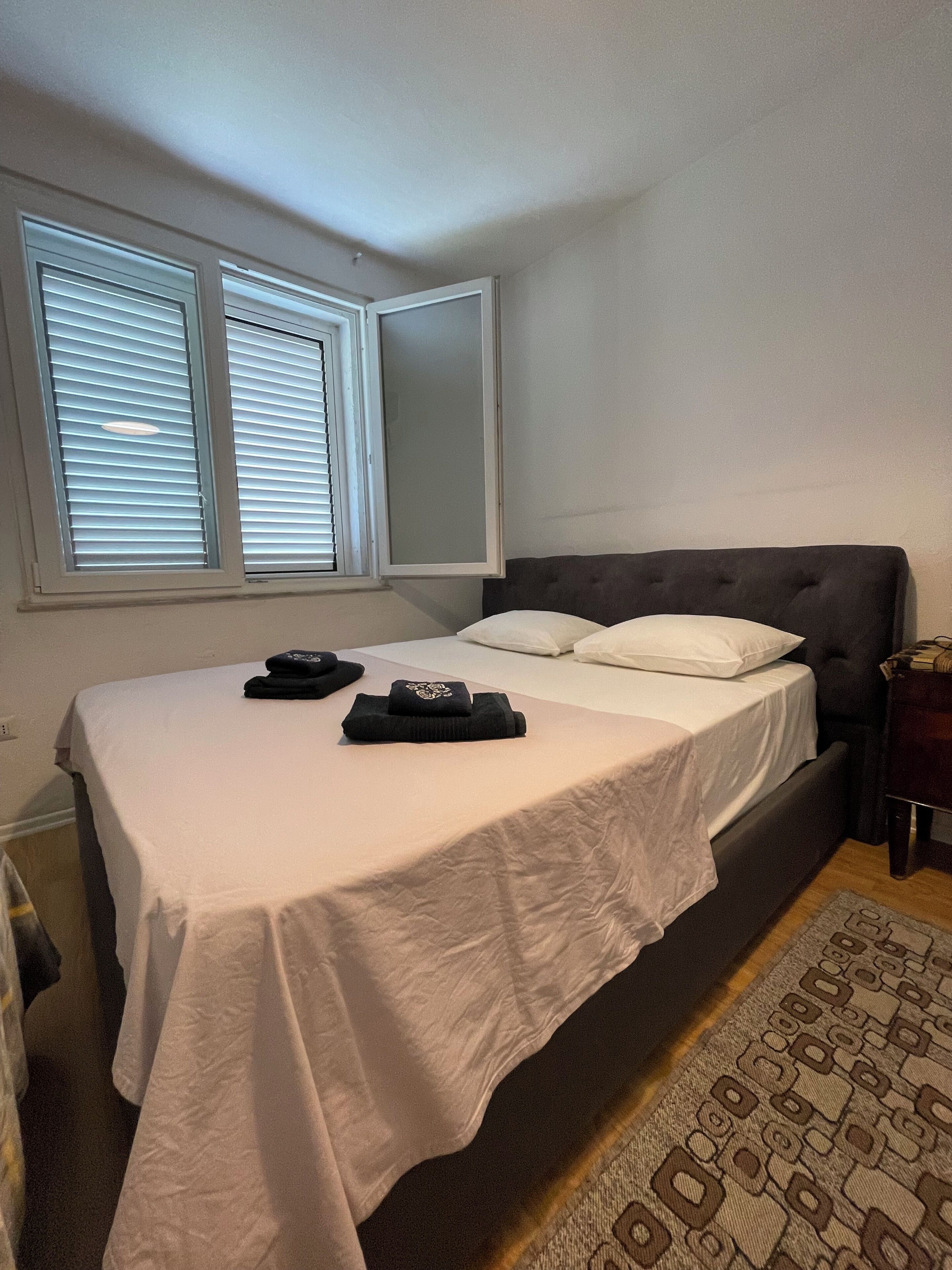 Una cama bien hecha con sábanas blancas, un cabecero oscuro y una mesita de noche con una lámpara.
