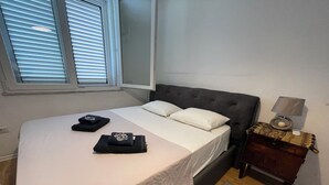 A neatly made bed with pillows and folded blankets, a bedside table with a lamp, and a patterned rug on a wooden floor.