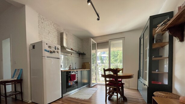 A modern kitchen with a built-in oven, a dining area with a wooden table and chairs, and a large window providing natural light.