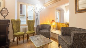 Una sala de estar acogedora con chimenea, dos sillones tapizados de color verde, un sofá gris y una mesa de centro con estampado.