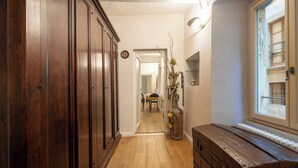 Un pasillo con suelo de madera, un mueble de madera grande, un baúl antiguo y una ventana con vistas al exterior.