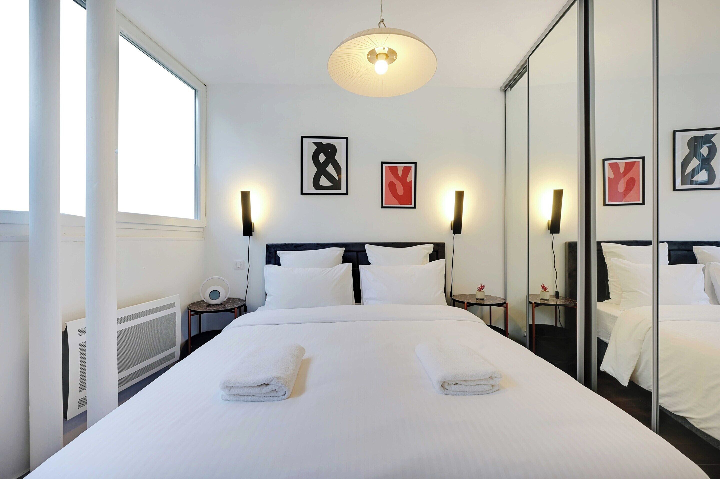 Habitació d'hotel amb un llit gran, dues taules de nit, una làmpada de nit, il·luminació fixada a la paret i obra emmarcada a la paret.