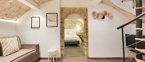 A room with a stone ceiling, a wooden staircase, a bed, a sofa, and a small stool.