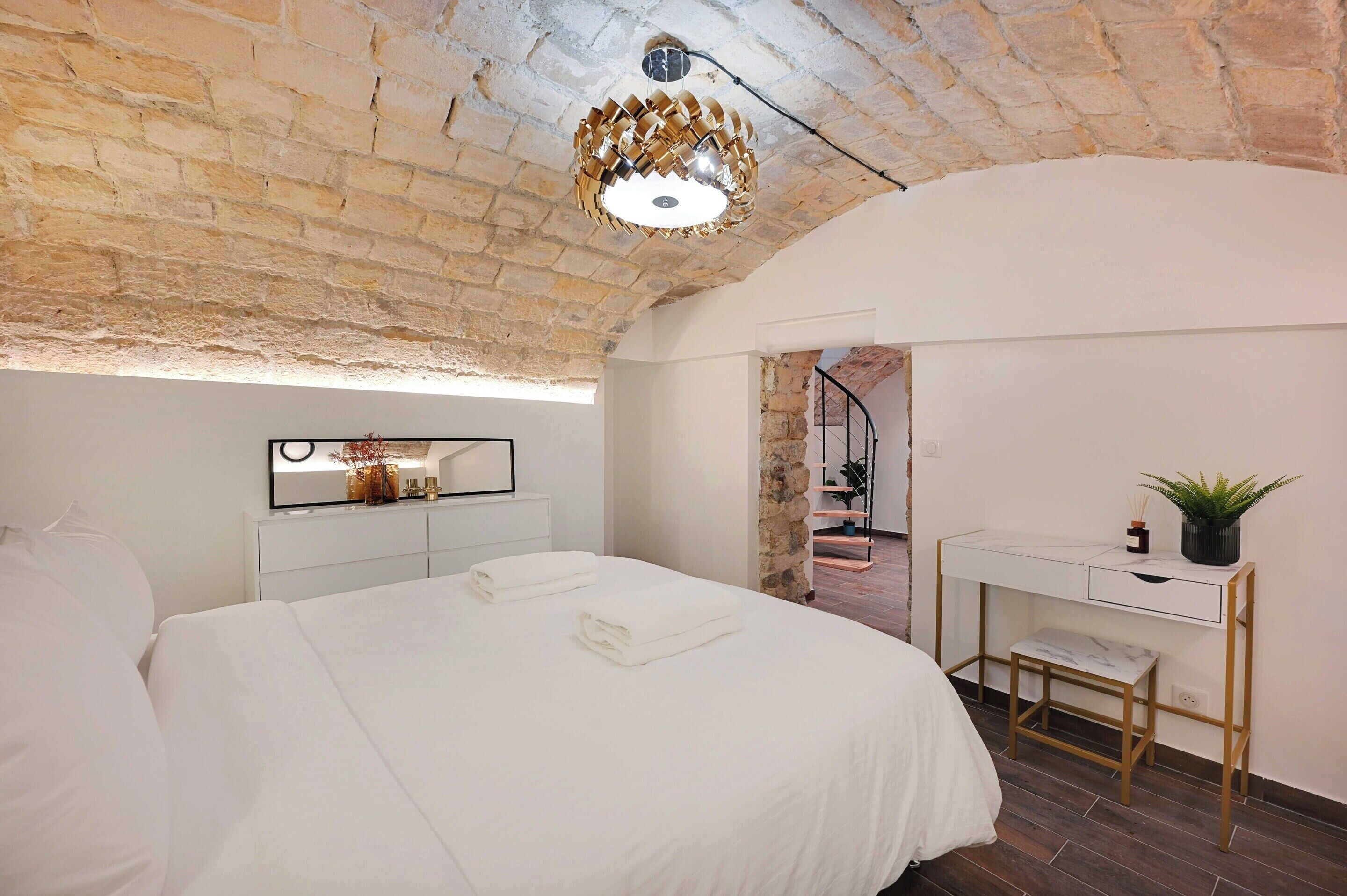 A bedroom with a large bed, a desk, and a stone wall.