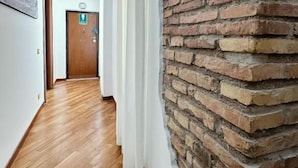 A hallway with wooden flooring, a brick wall, and a door with an emergency exit sign. - TIBERIM Exclusive Rome (Rome)