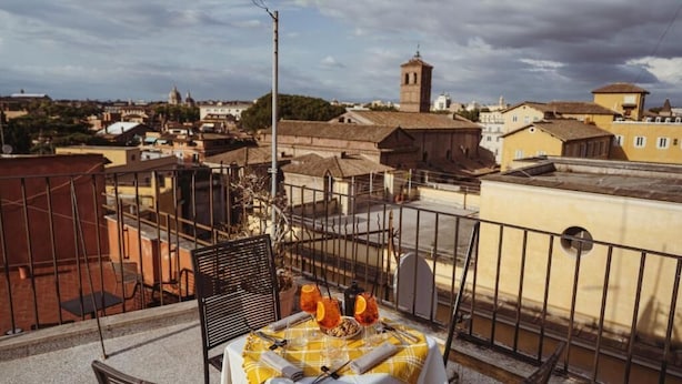 A rooftop terrace with a table set for two, overlooking a cityscape with historical buildings and a church tower. - TIBERIM Exclusive Rome (Rome)