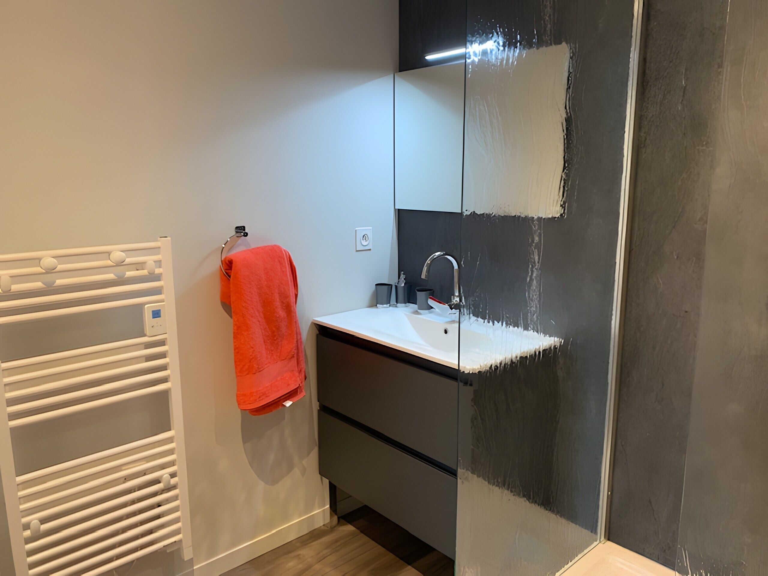 A bathroom with a white sink, a mirror, a towel rack with a red towel, and a white radiator.