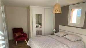 A bedroom with a bed, a red chair, a bedside table, a lamp, and a hanging light fixture.