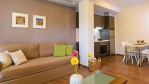 A modern living room with a sofa, a dining table with chairs, and a kitchen area. - Elounda Colour Apartments (Elounda)