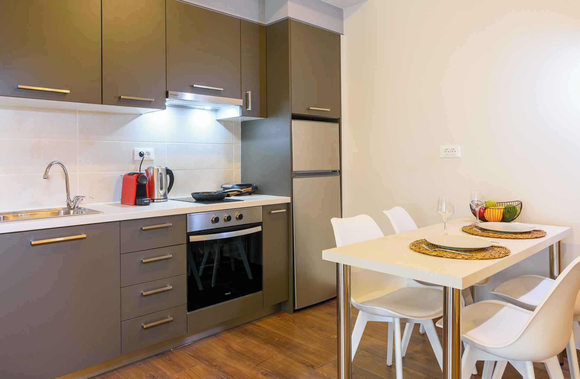 Une cuisine moderne équipée d’un four encastré, d’un réfrigérateur et d’un coin repas avec une table dressée pour deux personnes.