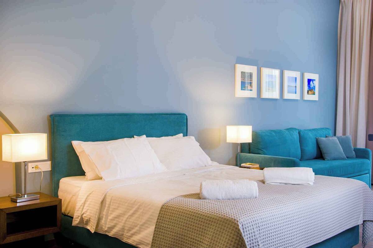 A hotel room with a bed, two bedside tables, a sofa, and a wall with framed pictures.