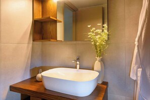 A bathroom with a white vessel sink, a wooden vanity, a mirror, and a vase with flowers. - Elounda Colour Apartments (Elounda)