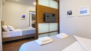 A hotel room with a bed, a TV mounted on a wooden panel, and two framed pictures on the wall. - Elounda Colour Apartments (Elounda)
