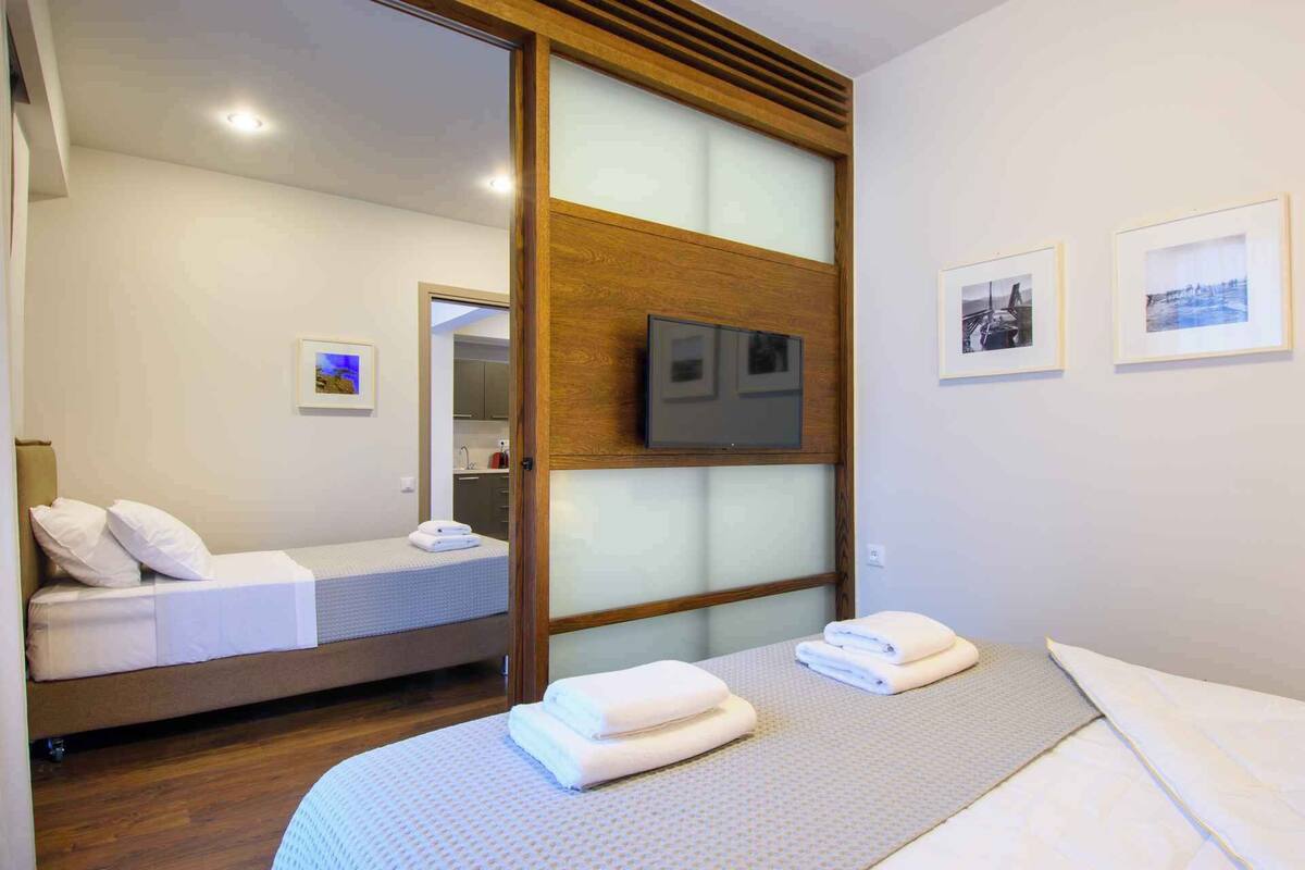 A hotel room with a bed, a TV mounted on a wooden panel, and two framed pictures on the wall.
