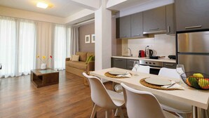 A modern kitchen with dark cabinets, a stainless steel refrigerator, and a dining area with a table set for two. - Elounda Colour Apartments (Elounda)