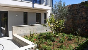 A modern building with a balcony, a garden with various plants, and a stone wall. - Elounda Colour Apartments (Elounda)