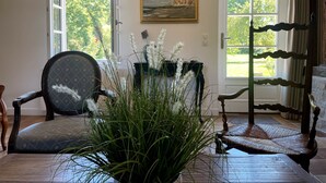 A room with a large window, a chair, a table, and a decorative plant. - Le Clos de Leger, a charming hamlet (Le Mesnil-Durdent)