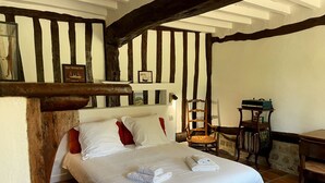 A traditional room with exposed wooden beams, a bed with white linens and red pillows, a wooden chair, a small table with a green tray, and a wall-mounted picture frame. - Le Clos de Leger, a charming hamlet (Le Mesnil-Durdent)