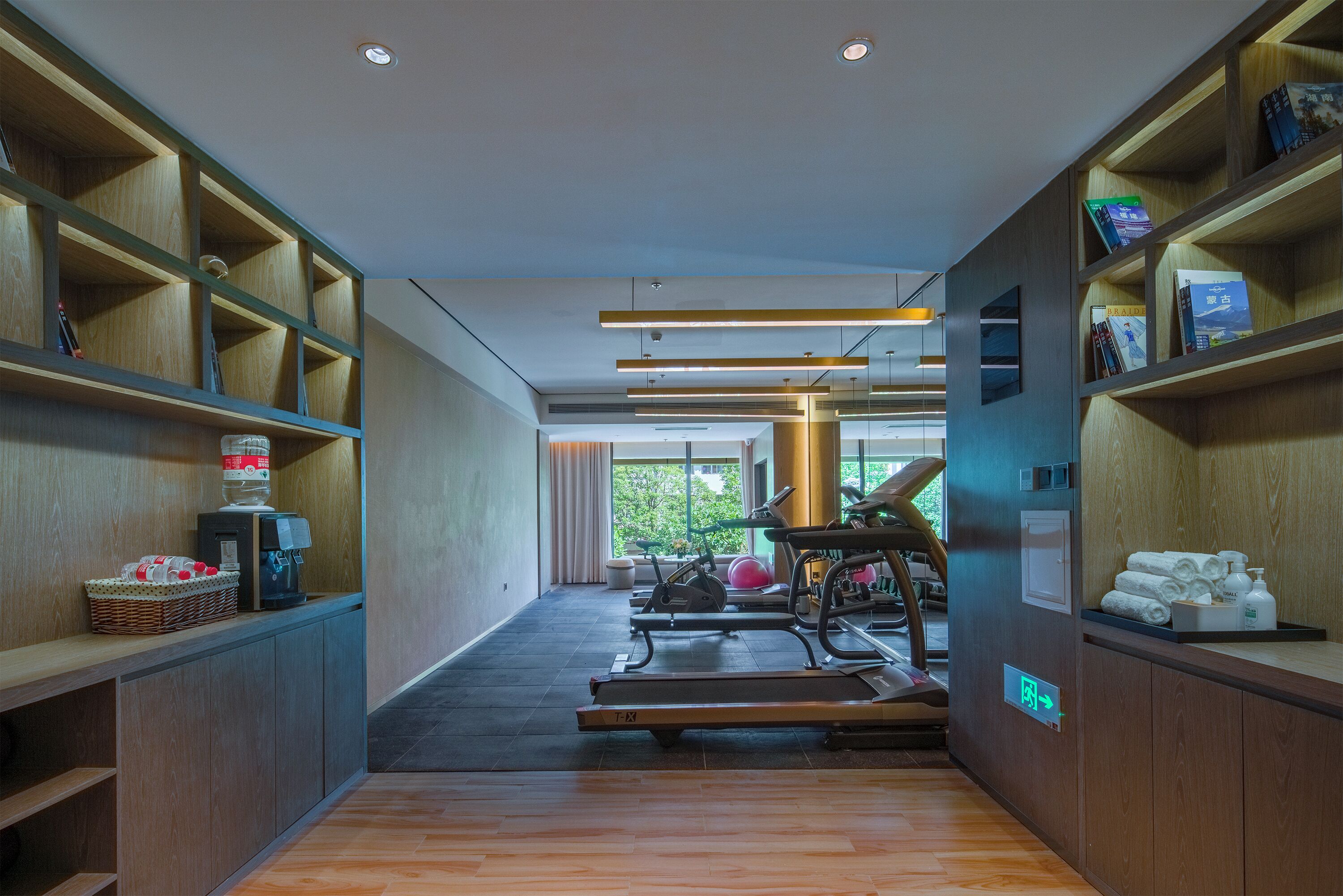 A gym with exercise equipment, wooden shelves, and a view of greenery outside.