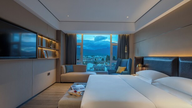 Een moderne hotelkamer met een groot bed, een sofa, een televisie en uitzicht op de stad.