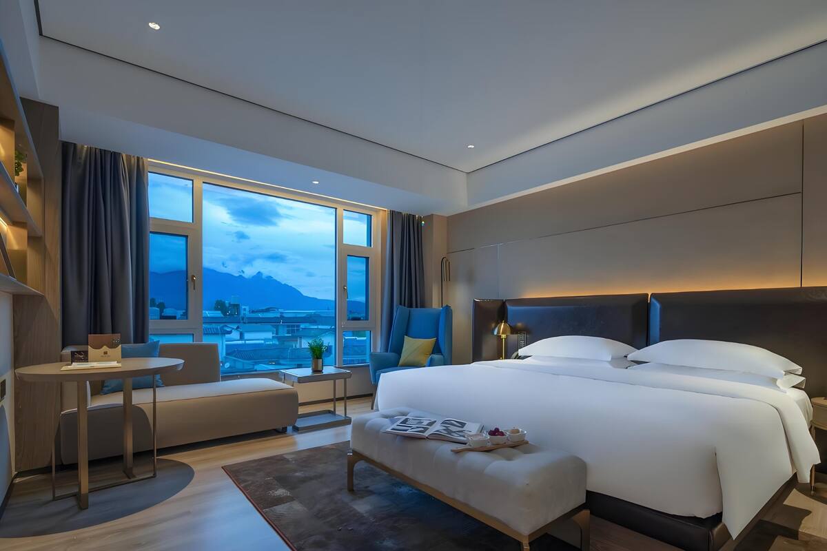 Una habitación de hotel moderna con una cama grande, un área de descanso y vistas a la ciudad.