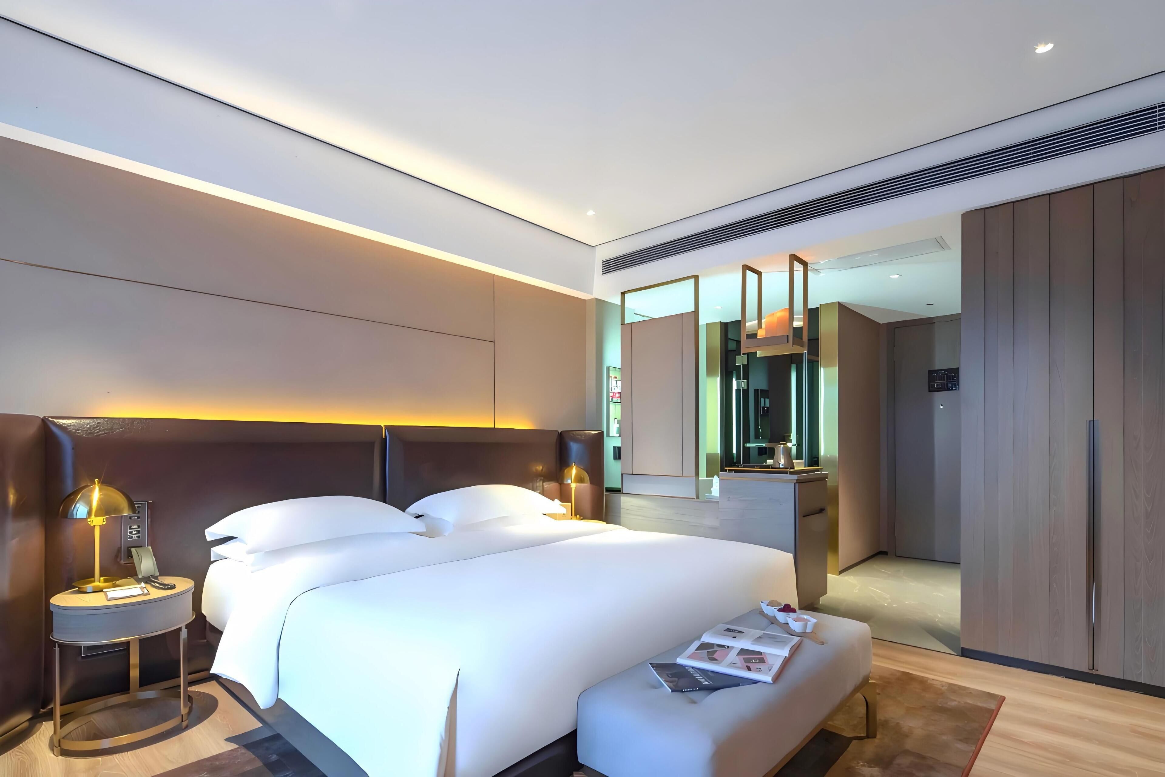 A modern hotel room with a large bed, bedside tables, a small desk, and a mirror.
