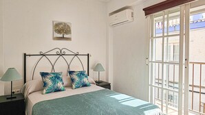 Ein Schlafzimmer mit einem Bett, zwei Nachttischen, einer Wand-Klimaanlage, einem Fenster mit Blick und einer Tür.