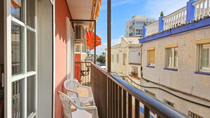 Ein Balkon mit zwei weißen Plastikstühlen, einem roten Sonnenschirm und Blick auf benachbarte Gebäude.