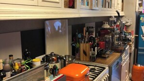 Une cuisine avec des meubles blancs, une cuisinière à gaz, un four et un tapis rayé aux couleurs vives.