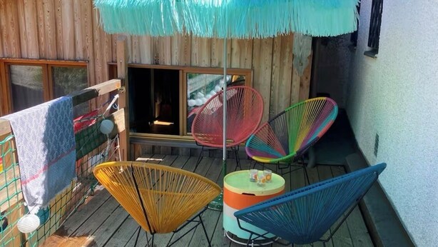 Une terrasse en bois avec un parasol en chaume, des chaises colorées et une petite table.
